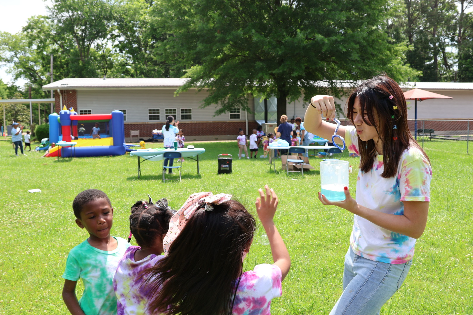 Kitty facilitating an outdoor STEM activity with children wearing tie-dye shirts